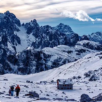 Two people walking outside of a cottage in a snowy mountain range